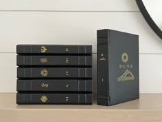 four black books sitting next to each other on a wooden table in front of a clock