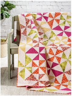 a colorful quilt sitting on top of a wooden bench next to a potted plant