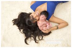 a woman holding a baby in her arms while laying on top of a white blanket