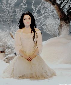 a woman sitting in the snow wearing a white dress