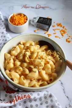 a white bowl filled with macaroni and cheese on top of a table next to a spoon