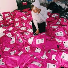 a woman in white hoodie and black pants surrounded by pink plastic bags with tags on them