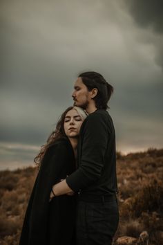 a man and woman embracing in the middle of a field with dark clouds above them