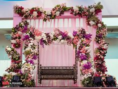 a bench covered in flowers next to a pink backdrop with white and purple flowers on it