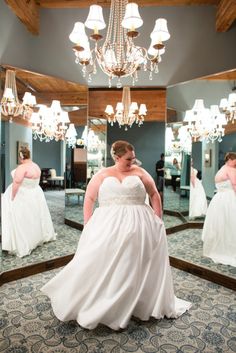 a woman standing in front of a mirror wearing a wedding dress and looking at her reflection