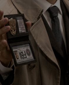 a man in a trench coat holding up two small badges that say libi on them