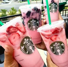 three drinks with strawberries and blueberries in them are being held up by someone's hand