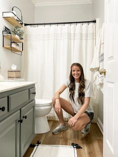 a young woman sitting on the floor in front of a bathroom sink and shower curtain