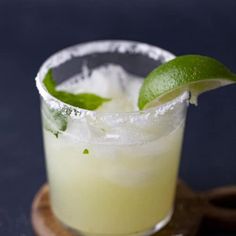 a close up of a drink on a wooden tray with a lime slice and salt