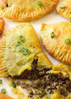 several pastries on a white surface with green onions and meat in the crusts