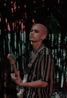 a man playing an electric guitar in front of some trees and palm trees at night