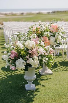 an outdoor ceremony setup with white chairs and flowers in vases on the grass at the end of the aisle