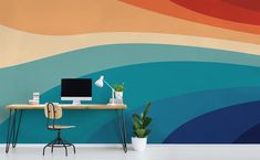 a desk with a computer on it in front of a wall painted with multicolored waves