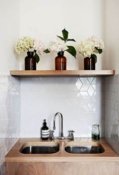 three vases with flowers sit on top of a shelf above a kitchen sink