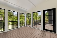 an empty room with large windows and wood flooring on the outside, looking out onto a wooded area