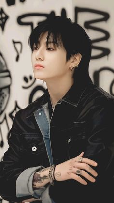 a man with black hair and piercings standing in front of a wall