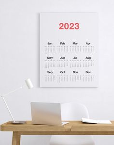 a desk with a laptop on it and a calendar hanging on the wall above it