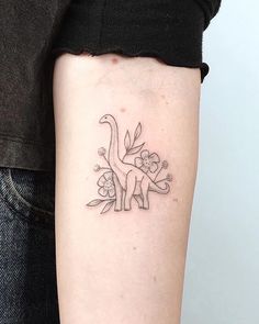 a small dinosaur tattoo on the left inner arm and lower arm, with flowers around it