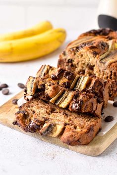 sliced loaf of chocolate chip banana bread sitting on a cutting board next to two bananas