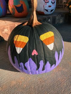 a painted pumpkin sitting on the ground next to other decorated pumpkins in different colors