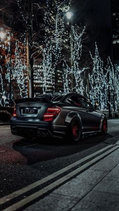 a black sports car parked on the side of the road at night with christmas lights in the background