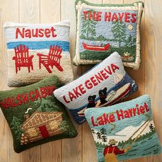 four decorative pillows with embroidered sayings on them sitting on a wooden floor in front of a wood paneled wall