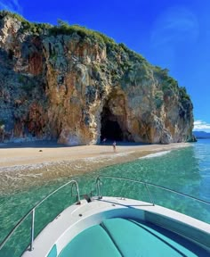 a boat traveling past a cave on the beach