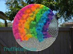 a rainbow colored glass plate sitting on top of a wooden table next to a tree