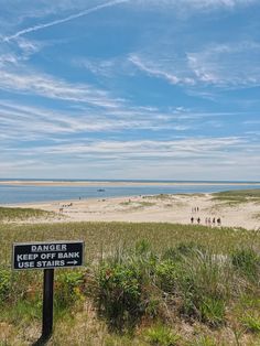 a sign that is on the side of a beach near grass and people in the water