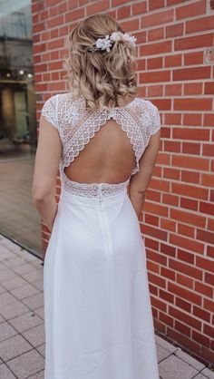 a woman in a white dress is standing near a brick wall with her back to the camera