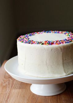 a white cake with colorful sprinkles on it sitting on top of a wooden table