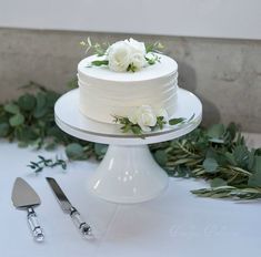 a wedding cake with white flowers on top and greenery next to the cake stand