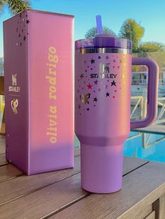 a purple travel mug sitting on top of a wooden table next to a pink box