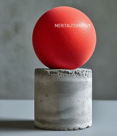 a red ball sitting on top of a cement block in front of a gray wall