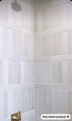 a white tiled bathroom with a gold faucet and shower head in the corner