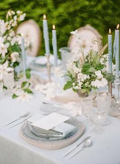 the table is set with silverware and white flowers, candles, and napkins