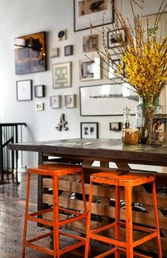 two orange stools sit in front of a wooden table with pictures on the wall