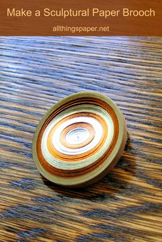 a paper brooch sitting on top of a wooden table with the words make a sculptural paper brooch