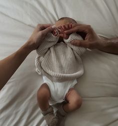 a baby being held up by two hands on top of a white sheet covered bed