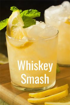 two glasses filled with ice and lemons on top of a wooden cutting board next to sliced