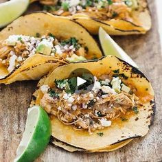 three tacos with shredded meat, cheese and cilantro on a cutting board