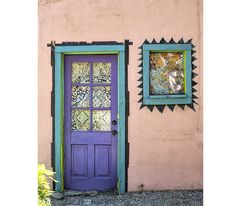 a purple door and window in front of a pink stucco wall with green trim on it