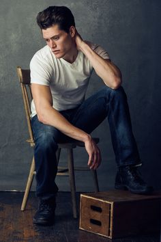 a man sitting on top of a wooden chair next to a box with his hand on his head