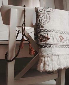 a white chair with a tasseled cushion on it's arm and a beaded necklace hanging from the back