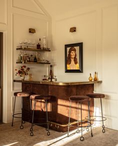 a bar with three stools in front of it and a painting on the wall