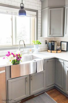 a kitchen with gray cabinets and white counter tops, flowers in the window sill