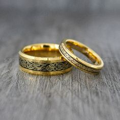 two gold wedding rings sitting on top of a wooden table next to each other,