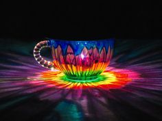 a colorful coffee cup sitting on top of a table next to a neon light fixture