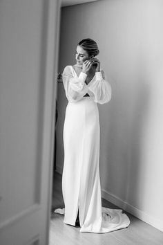 a woman standing in front of a mirror wearing a white dress and holding her hands to her face