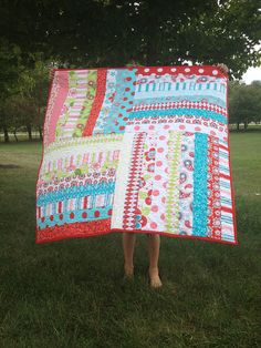 a woman standing in the grass holding up a quilt